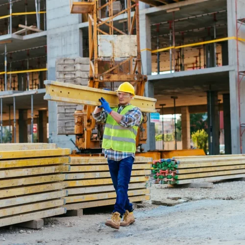 Homme portante une poutre sur un chantier de construction d'un immeuble